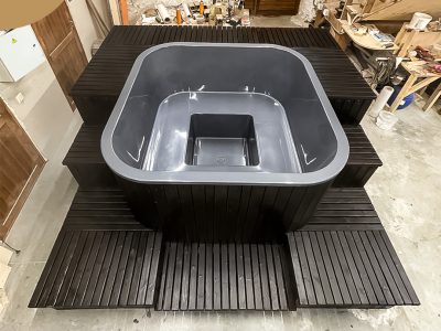 A square hot tub with a wrap-around stairs, finished with burned boards